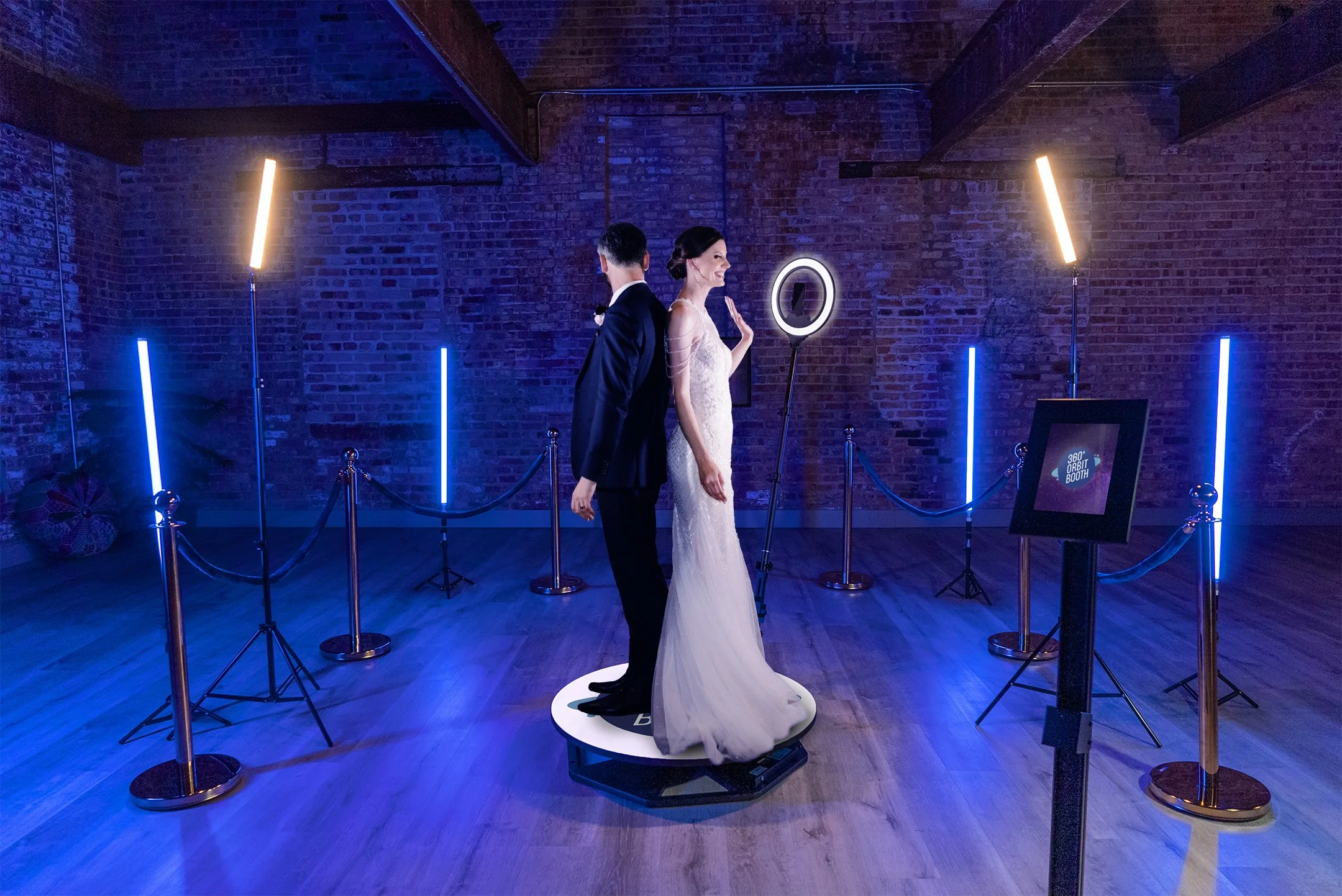 A couple standing on a 360 photo booth platform surrounded by LED lights at a wedding