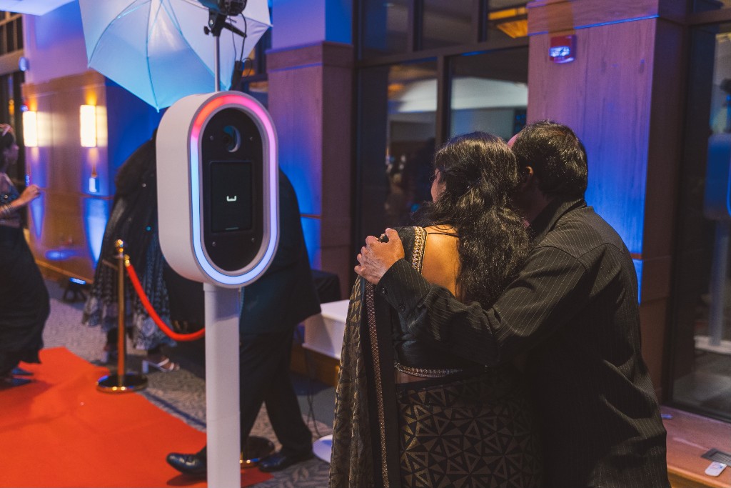 Guests posing beside an open-air FlicBox photo booth with a ring light and red carpet